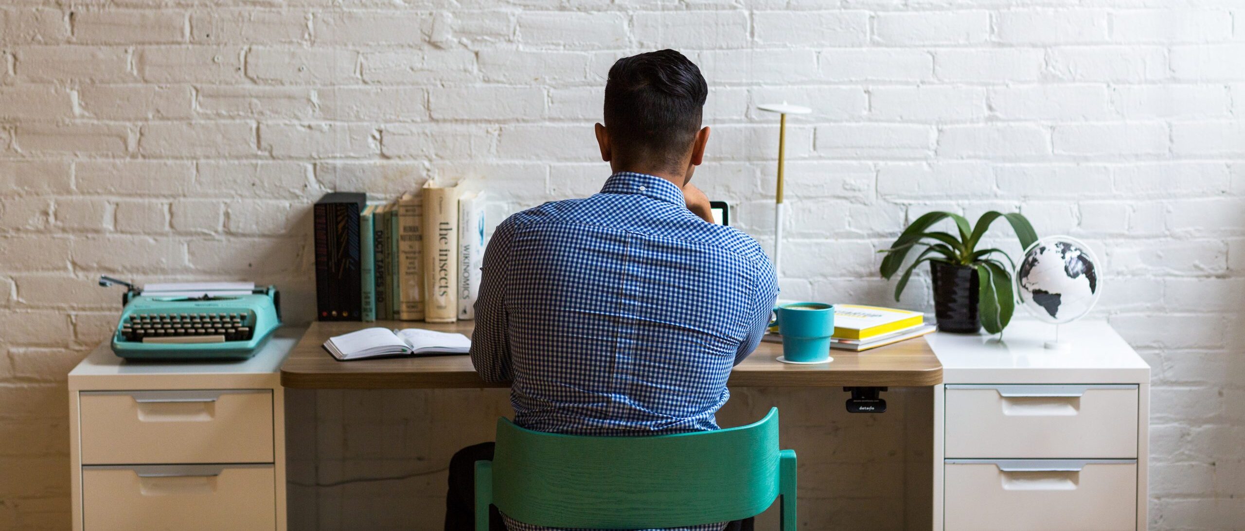Man working at a desk facing a white brick wall